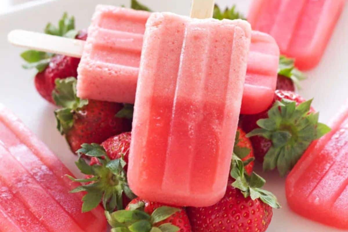 Several pink popsicles are arranged on top of fresh strawberries, with some popsicles partially eaten and others whole—showcasing a refreshing way to beat the heat and inspire new popsicle recipes.