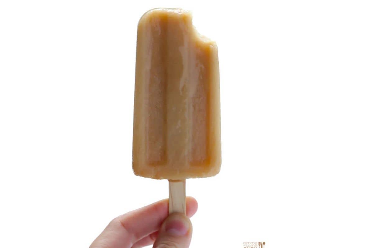 A hand holding a brown popsicle with a bite taken out of the top, against a white background—perfect to beat the heat with refreshing popsicles.