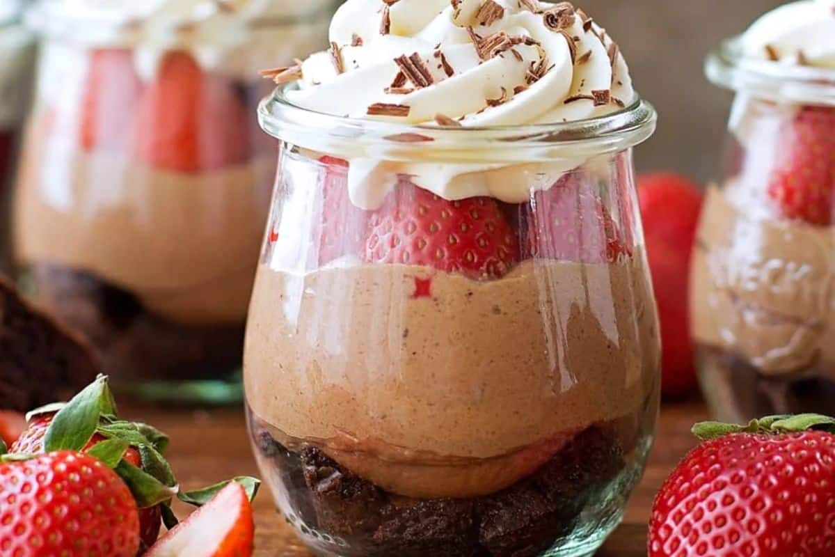 A glass jar filled with layers of brownie, chocolate mousse, whole strawberries, and topped with whipped cream and chocolate shavings—one of those Wow Desserts that's perfect for your summer dessert recipes collection.