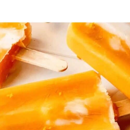 Three orange and white popsicles with wooden sticks lie on a light surface, with one partially bitten to reveal the inner texture—refreshing treats to beat the heat and inspire your next popsicle recipes.