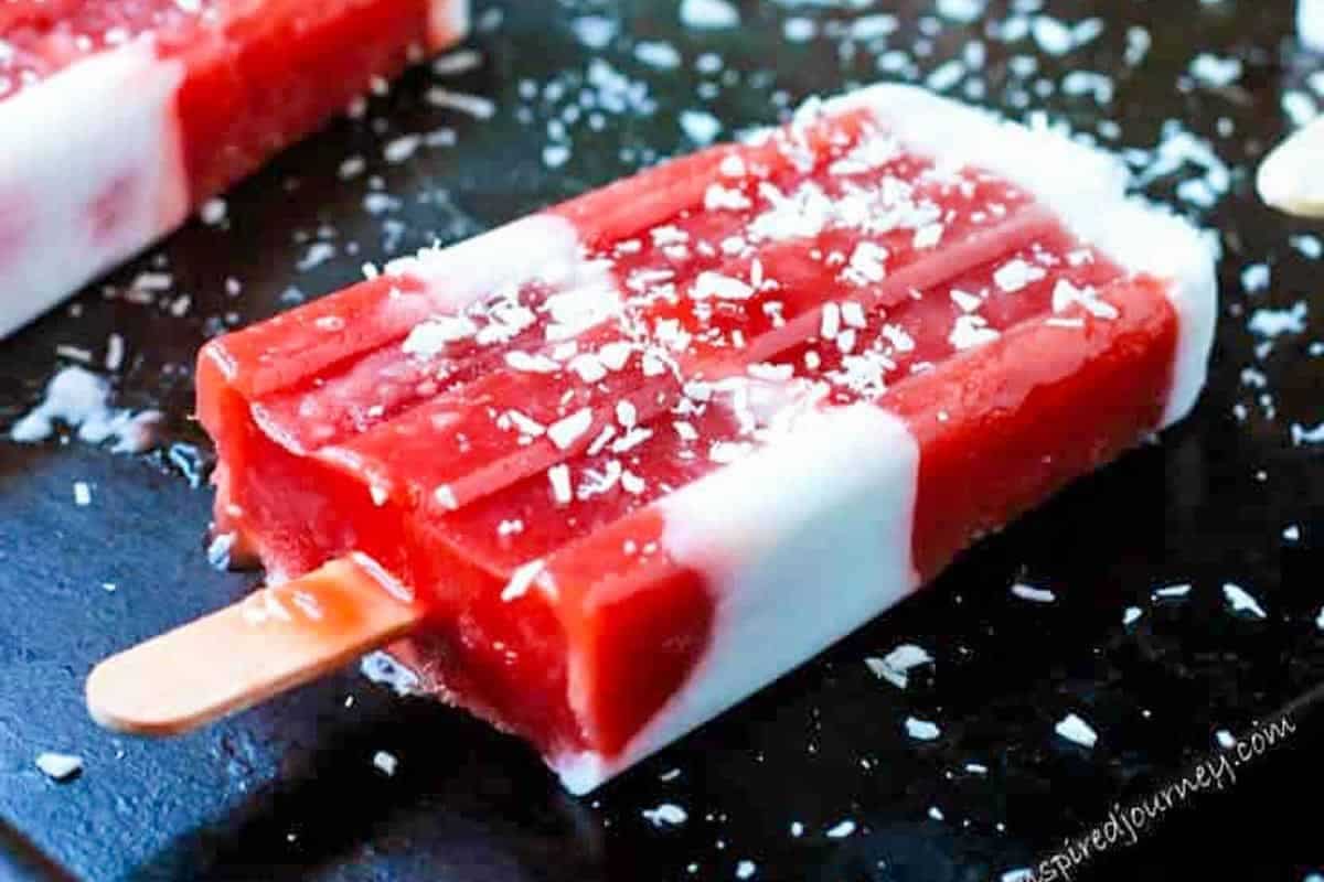 A refreshing red and white popsicle on a dark surface, sprinkled with shredded coconut—perfect to beat the heat and inspire new Popsicle recipes.