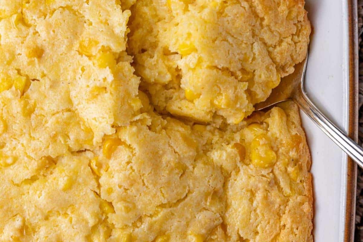 A close-up of baked cornbread casserole with a serving spoon lifting a portion from a rectangular dish—a comforting addition to your favorite summer recipes.