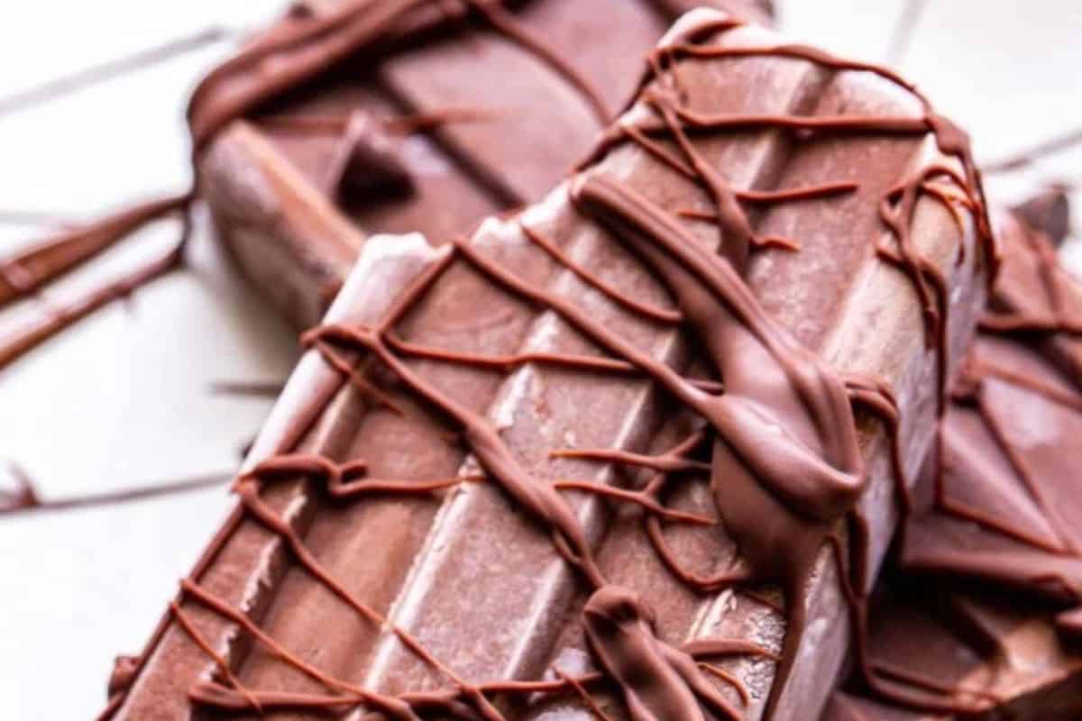Two chocolate popsicles are drizzled with melted chocolate on a white surface—perfect refreshing popsicles to beat the heat.