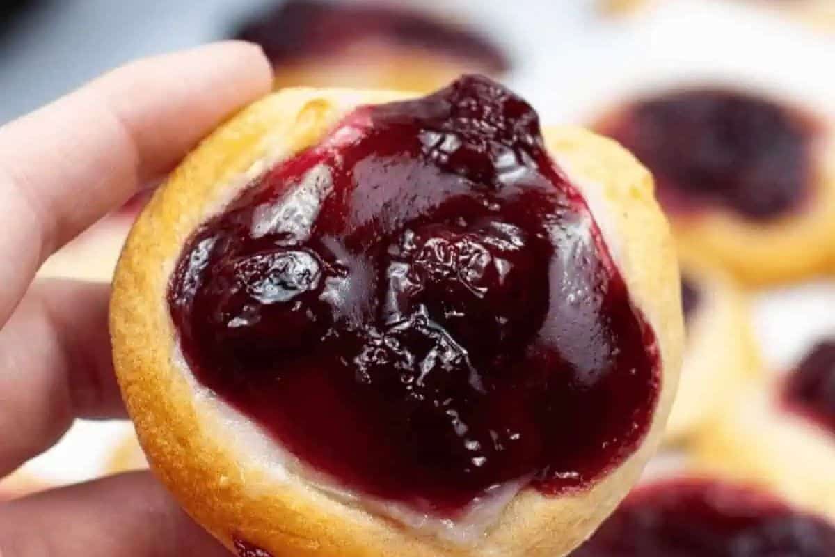 A hand holds a round pastry topped with glossy, dark red cherry filling—a tempting treat perfect for Fresh Cherry Recipes.