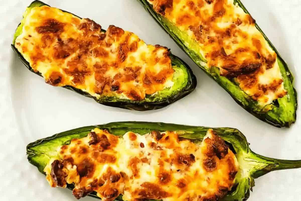 Three baked jalapeño halves filled with a creamy cheese mixture, topped with melted and browned cheese, make a spicy addition to your patriotic party foods—perfect for Labor Day or Memorial Day gatherings. Served on a white plate.
