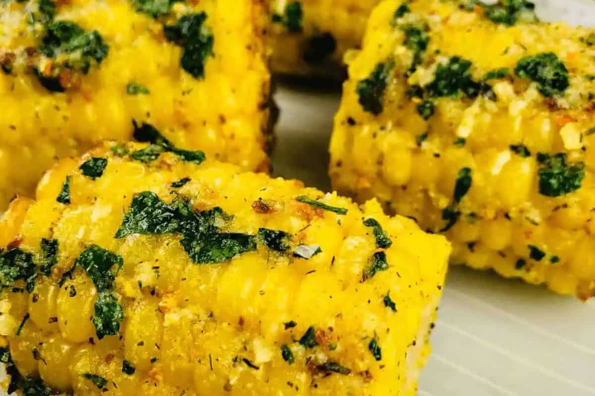 Close-up of corn on the cob pieces coated with herbs and seasoning, arranged on a light-colored surface—perfect inspiration for fresh summer recipes or creative corn recipes both on and off the cob.