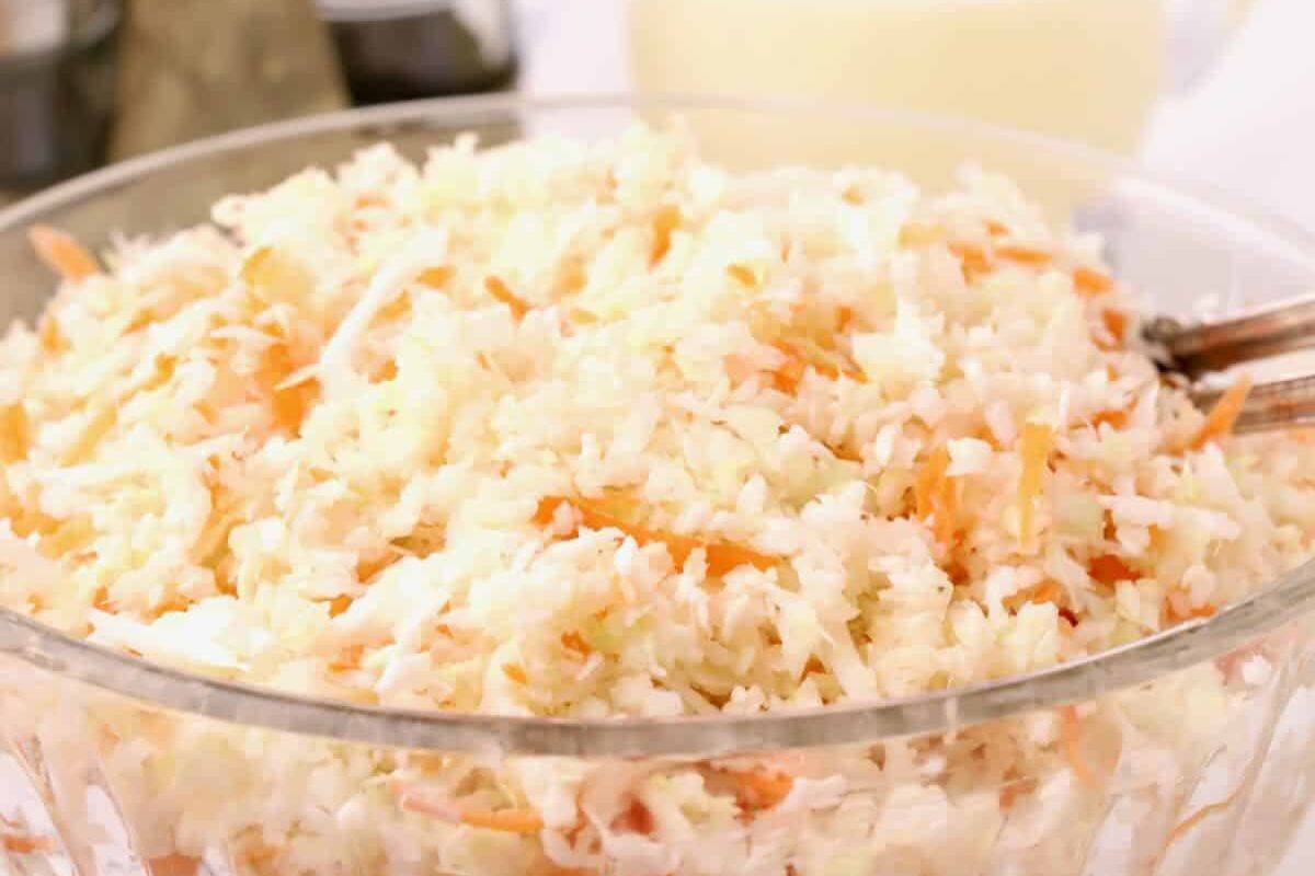 A clear glass bowl filled with finely shredded coleslaw—cabbage and carrots—awaits a serving utensil, making it a classic side for All American recipes and perfect for your next Star Spangled BBQ.