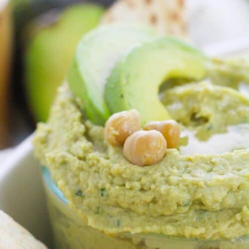 A bowl of creamy Avocado Hummus topped with sliced avocado and chickpeas, served alongside warm pita bread.