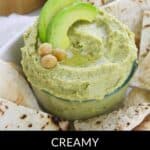 A bowl of creamy Avocado Hummus topped with avocado slices and chickpeas, surrounded by pieces of soft flatbread.