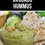 A bowl of creamy Avocado Hummus garnished with avocado slices and chickpeas, served alongside pieces of flatbread.