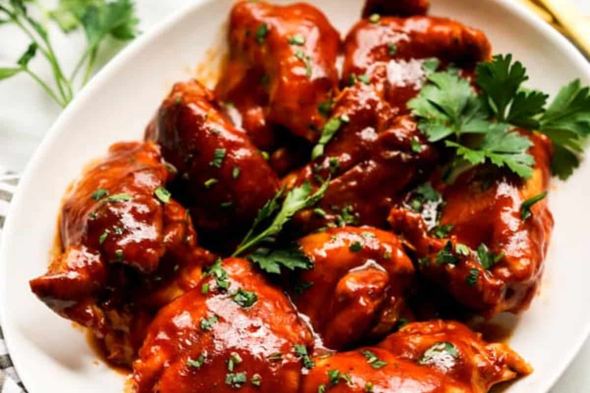 A white plate filled with glazed BBQ chicken pieces, garnished with chopped herbs and parsley—a star spangled twist on classic All American recipes.