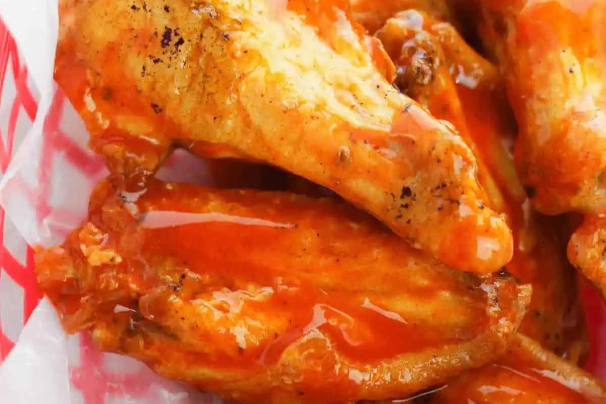 Close-up of several cooked chicken wings coated in a shiny orange sauce, served on a red and white paper tray—perfect for serving as patriotic party foods at your next Memorial Day or Labor Day gathering.
