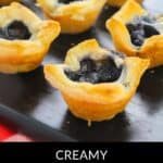 Several Mini Brie Bites with golden blueberry pastry crusts are arranged on a black serving tray.