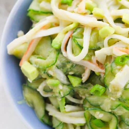 A close-up of a California Roll Cucumber Salad in a bowl, featuring sliced cucumbers, shredded crab sticks, and green onions mixed together.