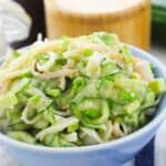 A blue bowl filled with California Roll Cucumber Salad—cucumber and shredded vegetables tossed in a creamy dressing—sits on a striped cloth.