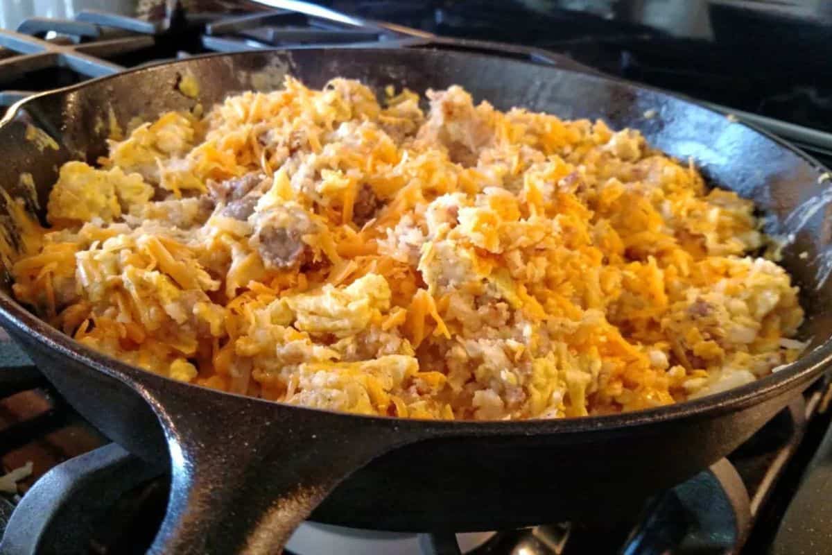 Scrambled eggs mixed with sausage and shredded cheddar cheese in a cast iron skillet on a stovetop—an easy and hearty camping meal perfect for your next outdoor adventure.