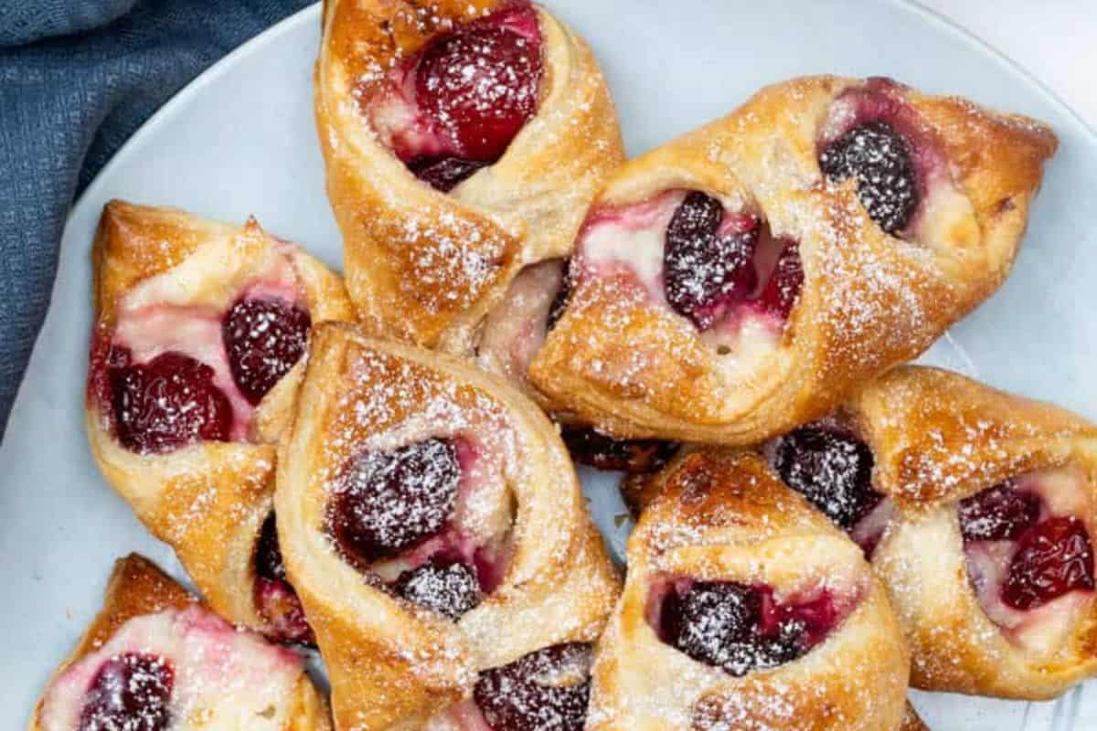 A plate of golden-brown pastries filled with cherries and dusted with powdered sugar, arranged closely together—perfect for those seeking fresh cherry recipes beyond pie.