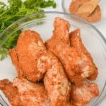 A glass bowl filled with raw chicken with coating.