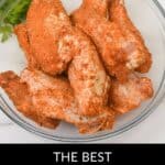 A glass bowl filled with raw chicken wings coated in a vibrant Chicken Wing Seasoning Rub, with parsley and extra seasoning in the background. Text at bottom reads: “The Best Chicken Wing Seasoning Rub.”.