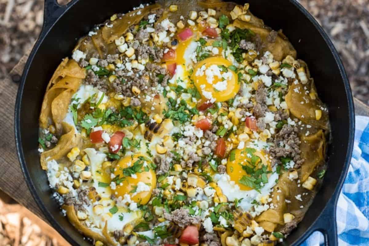 A flavor packed cast iron skillet filled with eggs, ground meat, tortilla chips, corn, cheese, diced tomatoes and chopped cilantro—perfect for trying out new camping recipes on your next camping trip.