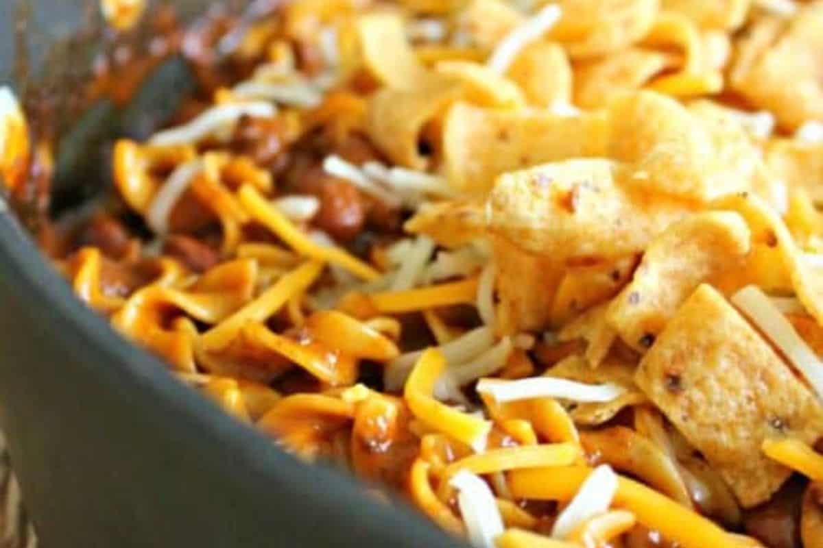 Close-up of a flavor packed dish featuring chili, shredded cheese and corn chips mixed together in a pan.