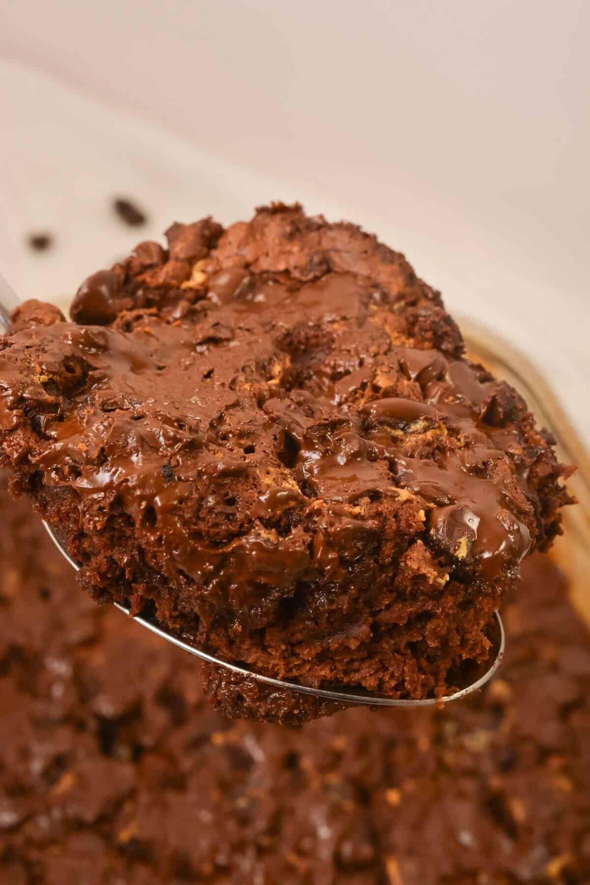 A close-up of a spoon holding the gooey, dessert above a tray of in the back.