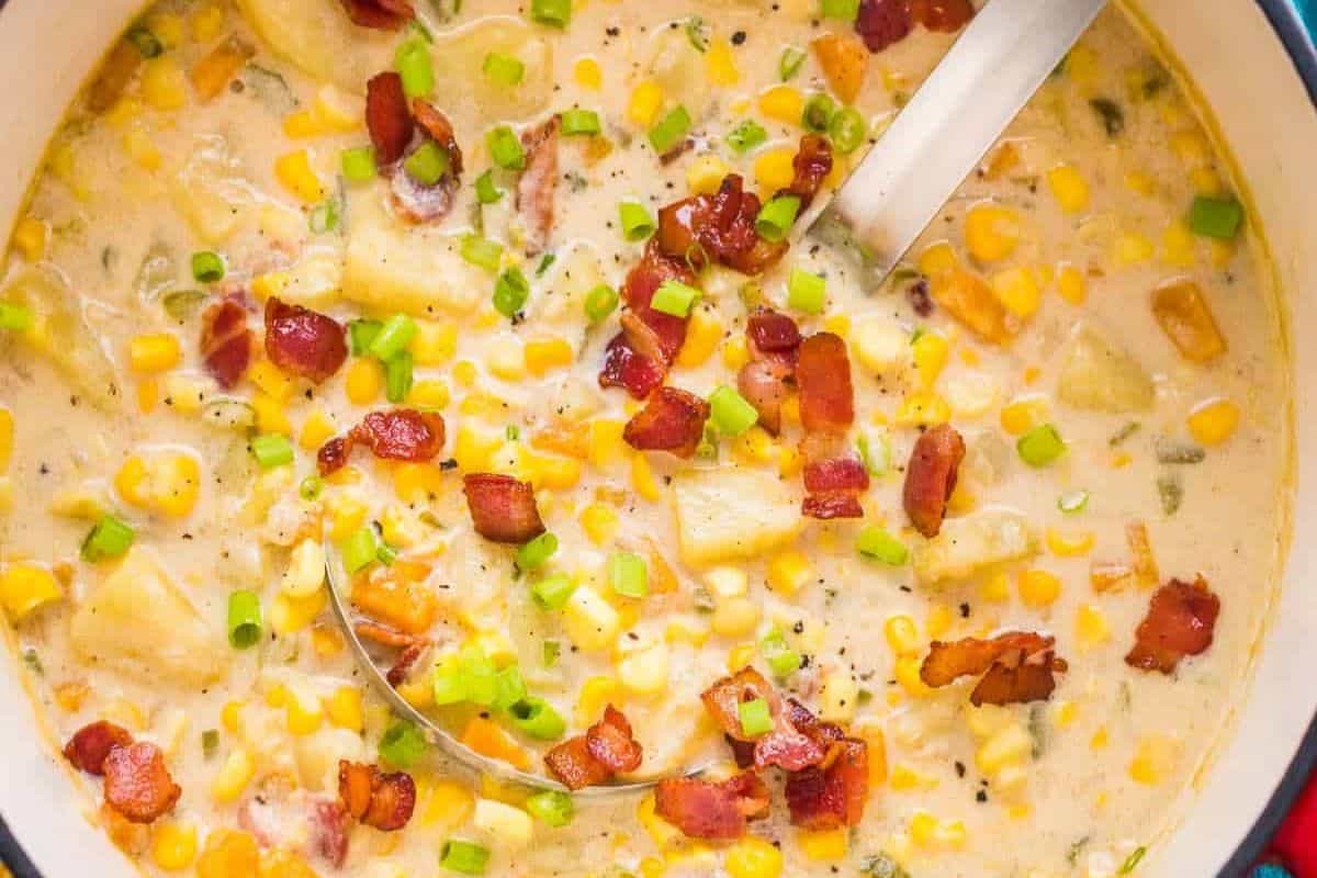 A pot of creamy corn chowder with diced potatoes, sweet corn, bacon pieces, and green onions—comfort in a bowl and one of the best corn recipes for summer. A ladle rests inside, ready to serve.