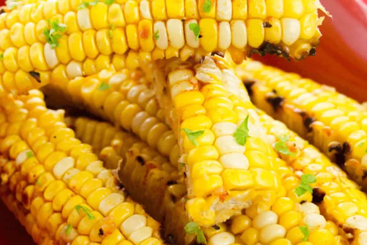 Grilled corn on the cob stacked on a plate, garnished with herbs—a delicious addition to your favorite summer recipes.