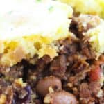 Close-up of a serving of tamale pie, similar to chili pie, with a cornbread topping, ground meat, beans, and vegetables on a red plate.