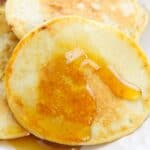 A stack of Cottage Cheese Oat Pancakes on a white plate with syrup drizzled on top.