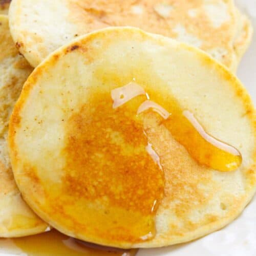 A stack of Cottage Cheese Oat Pancakes on a white plate with syrup drizzled on top.