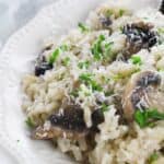 A close-up of creamy mushroom risotto garnished with grated cheese and chopped parsley on a white plate.
