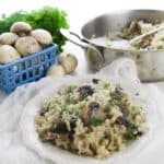 A plate garnished with herbs sits in front of a pan of the dish and a bunch of parsley on a white surface.
