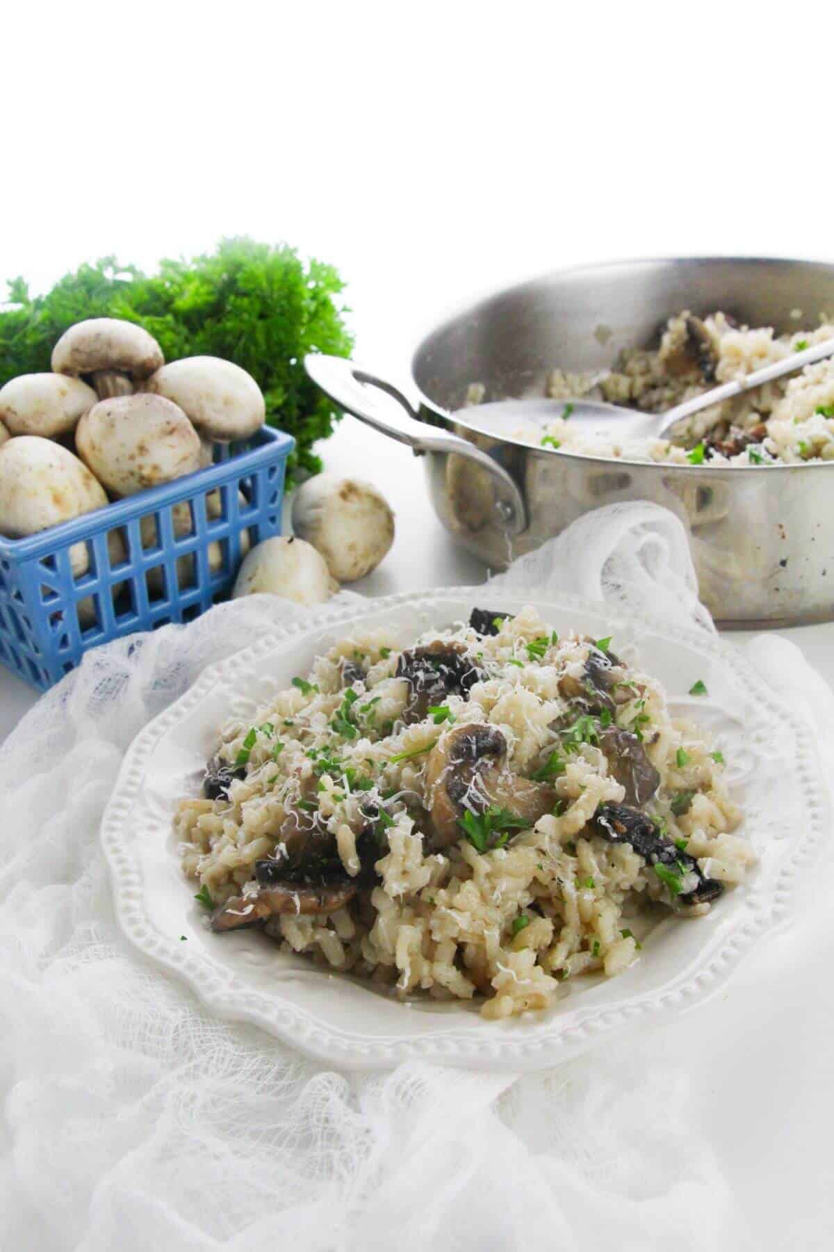 A plate garnished with herbs sits in front of a pan of the dish and a bunch of parsley on a white surface.