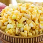 A brown bowl filled with a side featuring chopped eggs, celery, and possibly red onion, all tossed in a creamy dressing.
