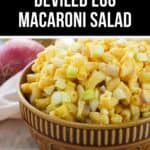 A brown bowl filled with Deviled Egg Macaroni Salad, featuring chopped eggs, macaroni, and green onions, with a red onion in the background.