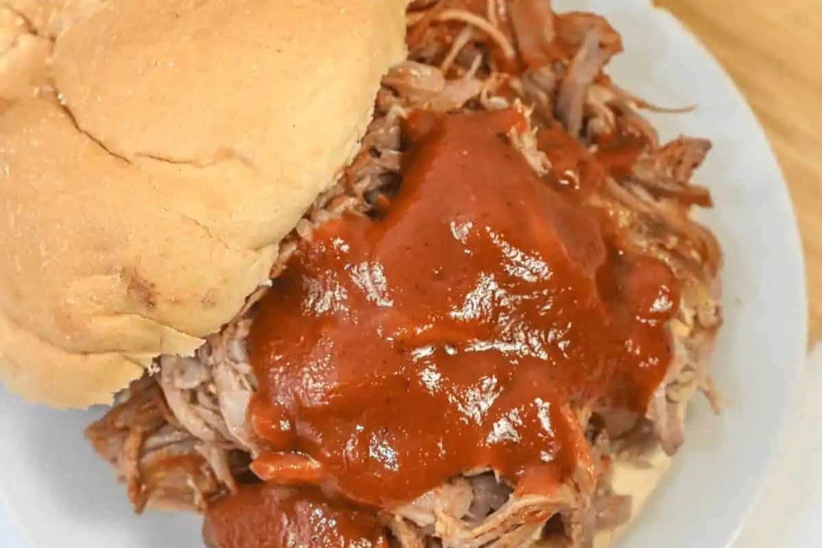 A pulled pork sandwich on a bun topped with barbecue sauce, served on a white plate—perfect for Labor Day or other patriotic party foods.