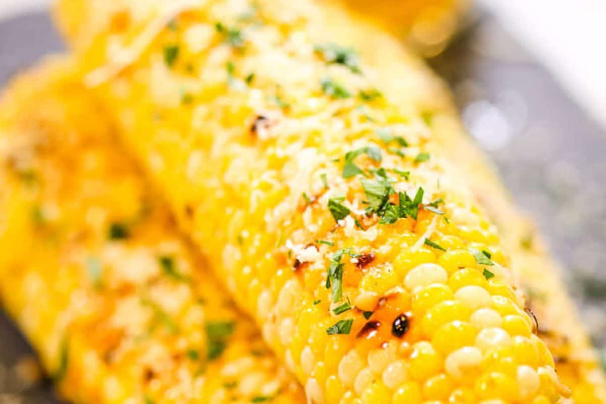 Close-up of corn on the cob topped with grated cheese and chopped herbs, with a light char visible on the kernels—perfect for summer recipes and those who love creative corn recipes.