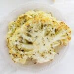 Two of the vegetables garnished with herbs and grated cheese are served on a white plate, with garlic and a wedge of cheese in the background, creating a savory vegetarian dish.