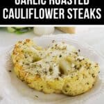 A serving of Roasted Cauliflower Steaks on a white plate, topped with herbs, sits against a rustic background, highlighting the savory garlic flavors.