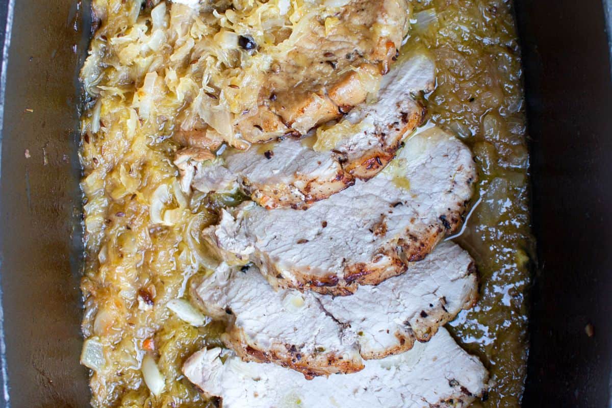 Sliced cooked pork roast served in a pan with sauerkraut and onions in a sauce—one of those German favorites that’s perfect for easy recipes or your next Oktoberfest celebration.