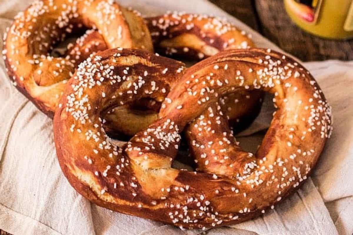Two soft pretzels topped with coarse salt rest on a beige cloth napkin, perfect for those seeking easy recipes or craving classic German favorites.