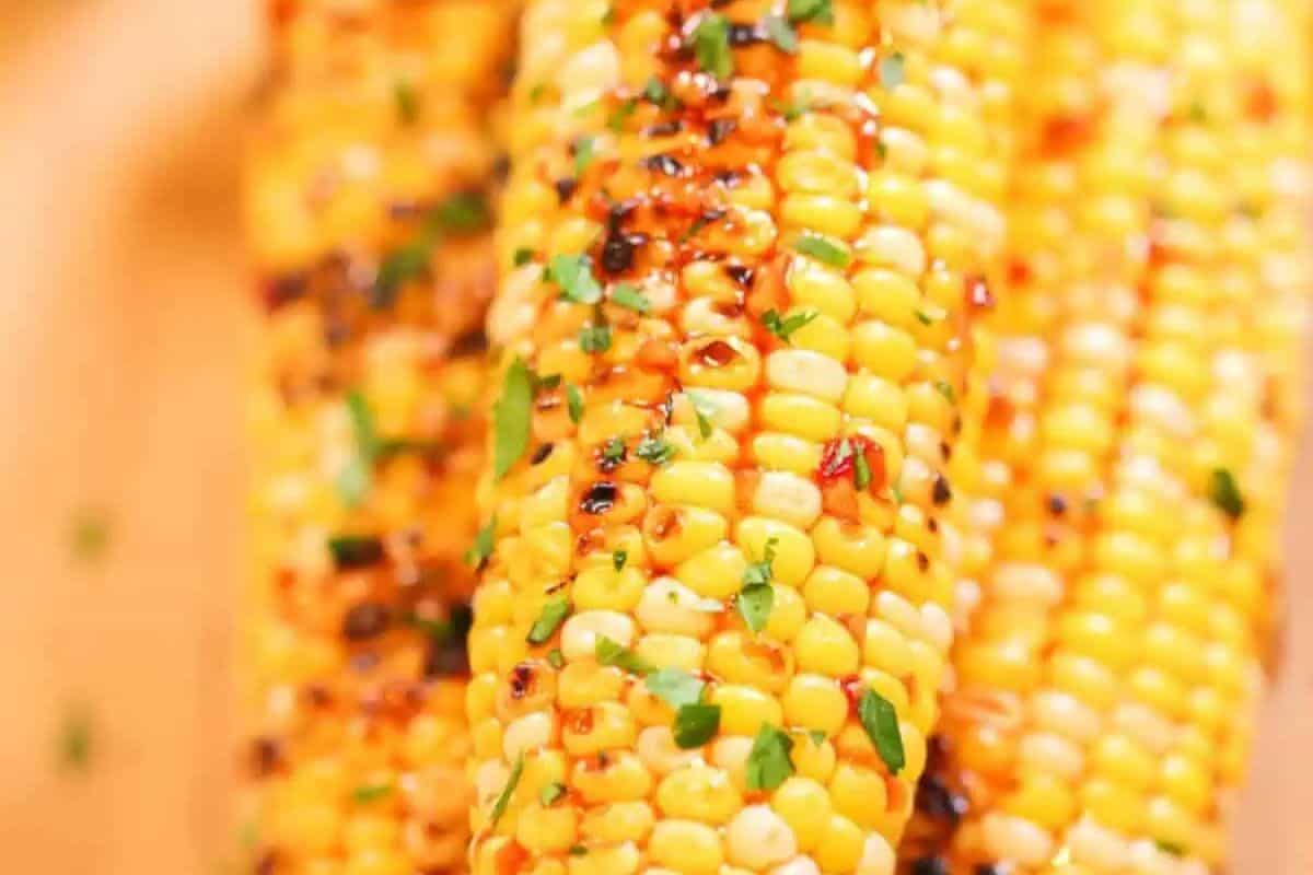 Grilled corn on the cob, a summer favorite, is topped with chopped herbs and seasoning, showcasing char marks and vibrant yellow kernels—a must-try for fans of classic corn recipes.