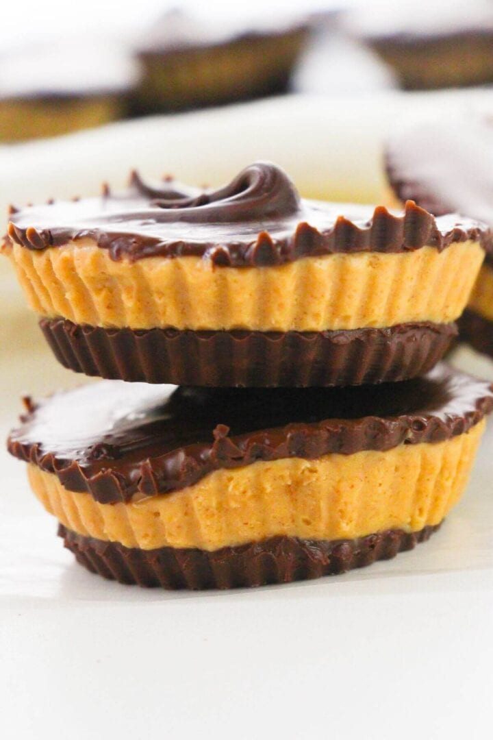 Two homemade peanut butter cups are stacked on top of each other, with a swirl of chocolate on the top cup, set against a blurred background.