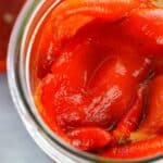 A close-up view of Roasted Red Bell Peppers packed in a glass jar with olive oil, showcasing their vibrant color and savory appeal.