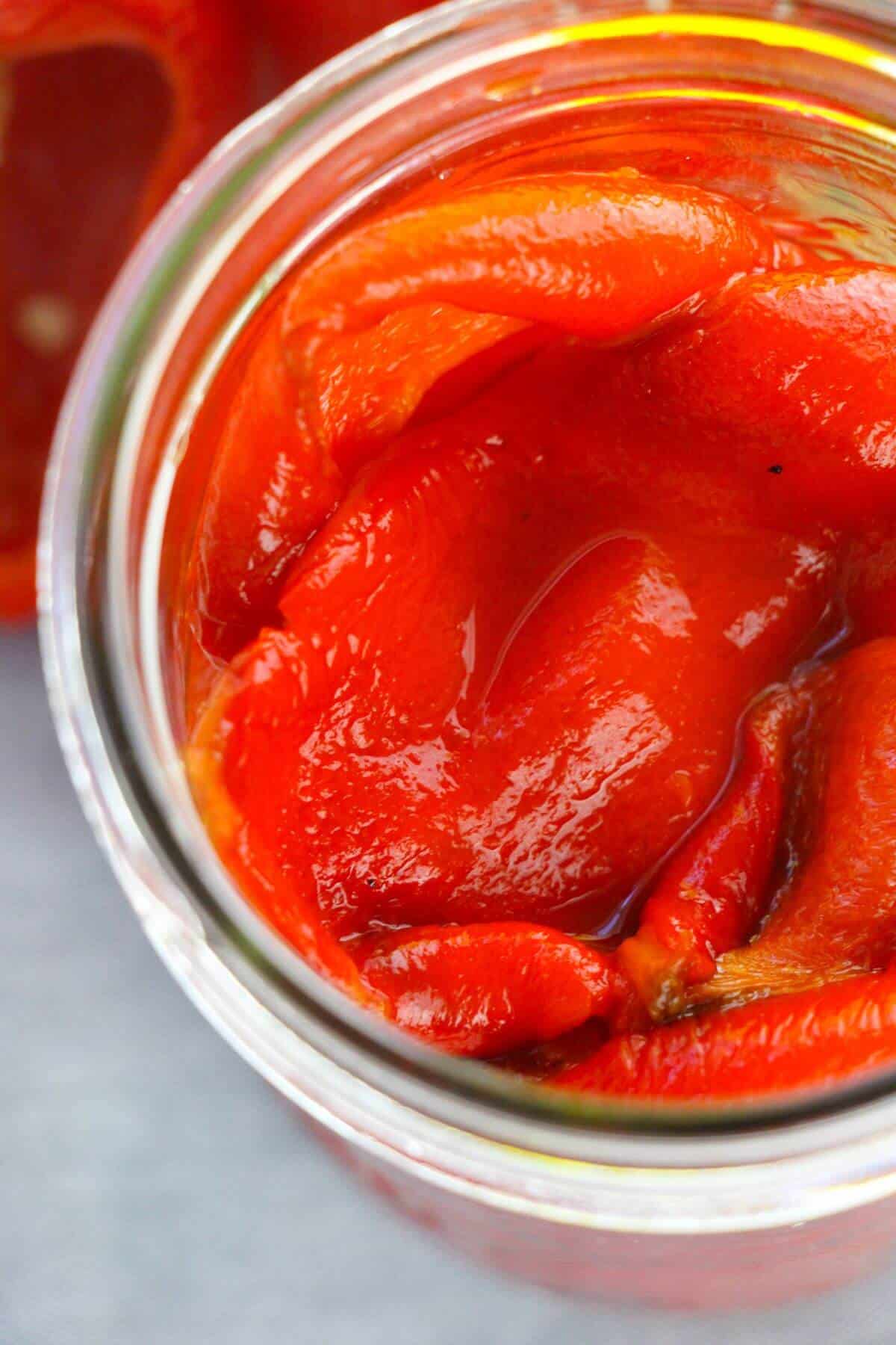 A close-up view of Roasted Red Bell Peppers packed in a glass jar with olive oil, showcasing their vibrant color and savory appeal.