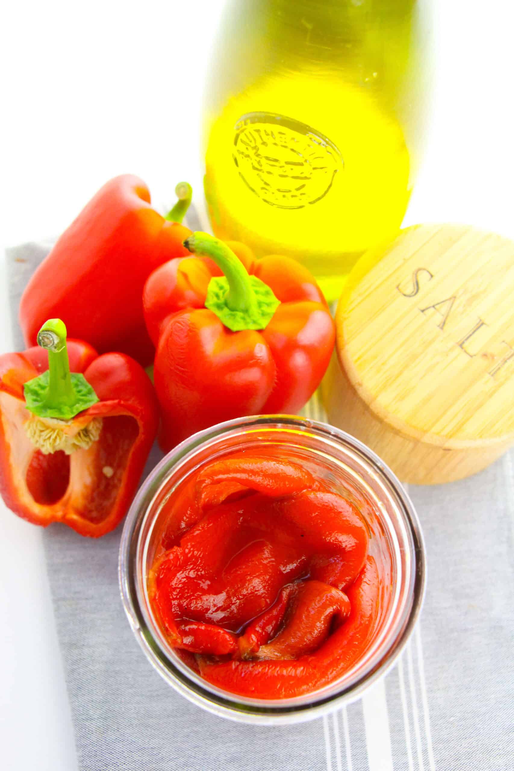Fresh veggies, a bottle of olive oil, and a wooden salt container are artfully arranged on a grey cloth.