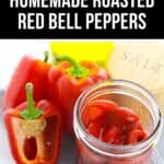 A jar of homemade Roasted Red Bell Peppers rests beside fresh red bell peppers and a salt container on a fabric surface.