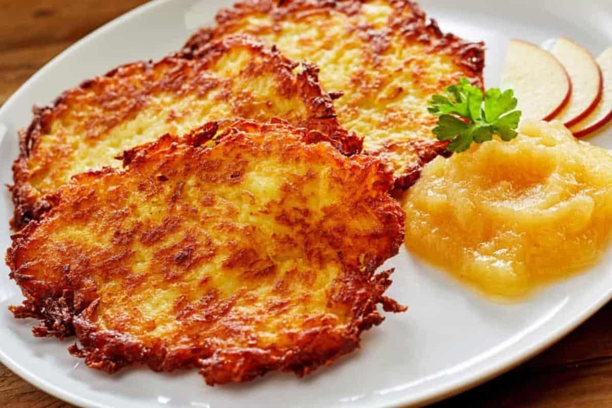 Three crispy potato pancakes on a white plate, served with applesauce, apple slices, and a parsley garnish—one of our German favorites that's perfect for Oktoberfest celebrations.
