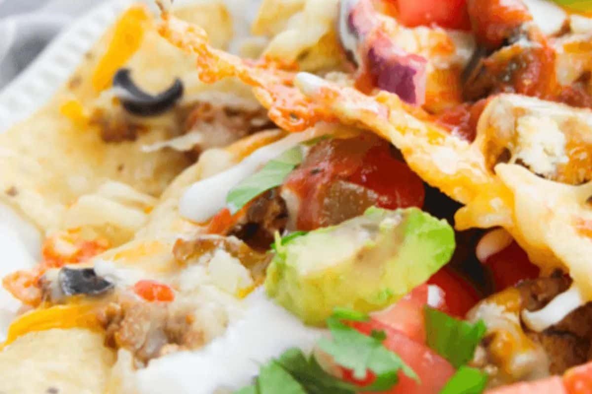 Close-up of loaded nachos topped with melted cheese, ground meat, avocado, tomato, black olives, and cilantro—perfect for your Memorial Day or Labor Day patriotic party foods table. Drizzled with white sauce for extra flavor.